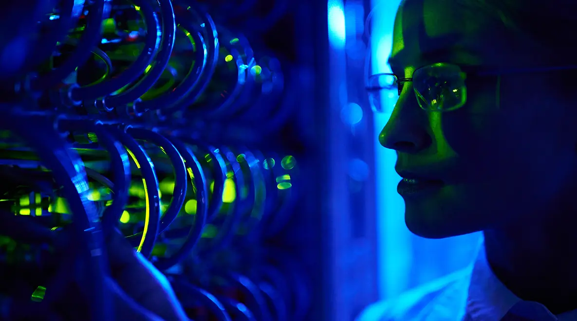 Close-up of a female computer scientist examining hardware in a blue-lit quantum computing lab.