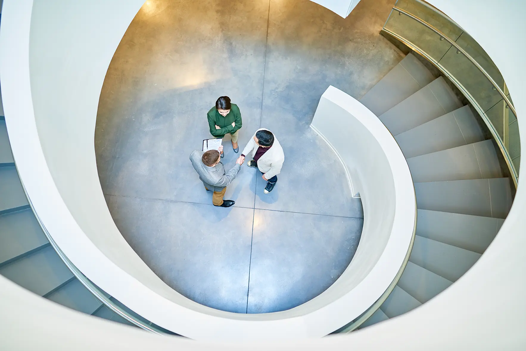 Three professionals standing in a circular space, shaking hands inside a modern spiral staircase