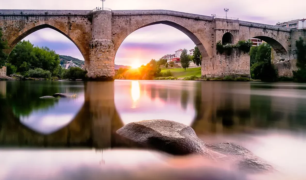 Old stone bridge over calm river at sunrise, symbolising enduring foundations and quiet strength.