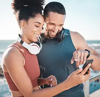 Fit couple smiling while checking a smartphone during an outdoor workout by the sea