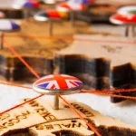 Pin with UK flag connected by red threads on a wooden map of Europe.