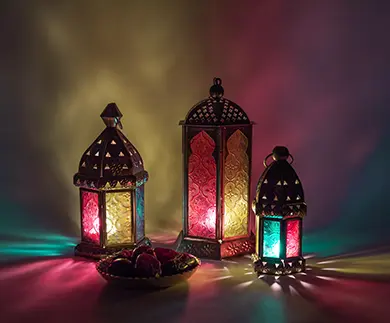 Three ornate Arabic lanterns lit with coloured lights casting soft shadows, with a bowl of dates beside them.